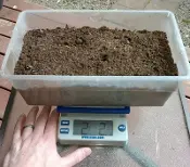 A person measuring soil in the plastic tub