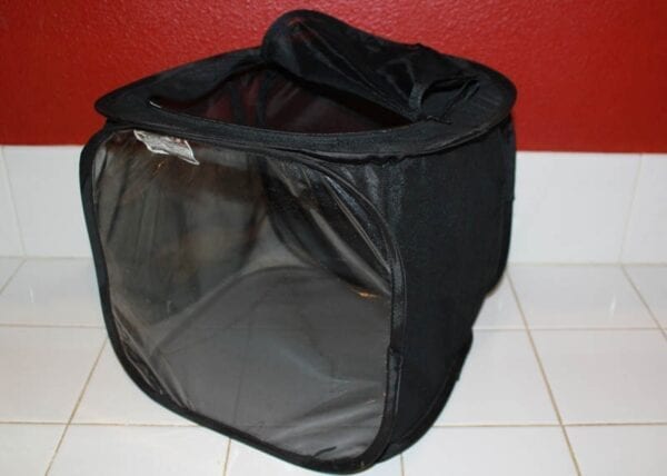 A Small Black Cube Net Mesh Cage sitting on a tile floor.